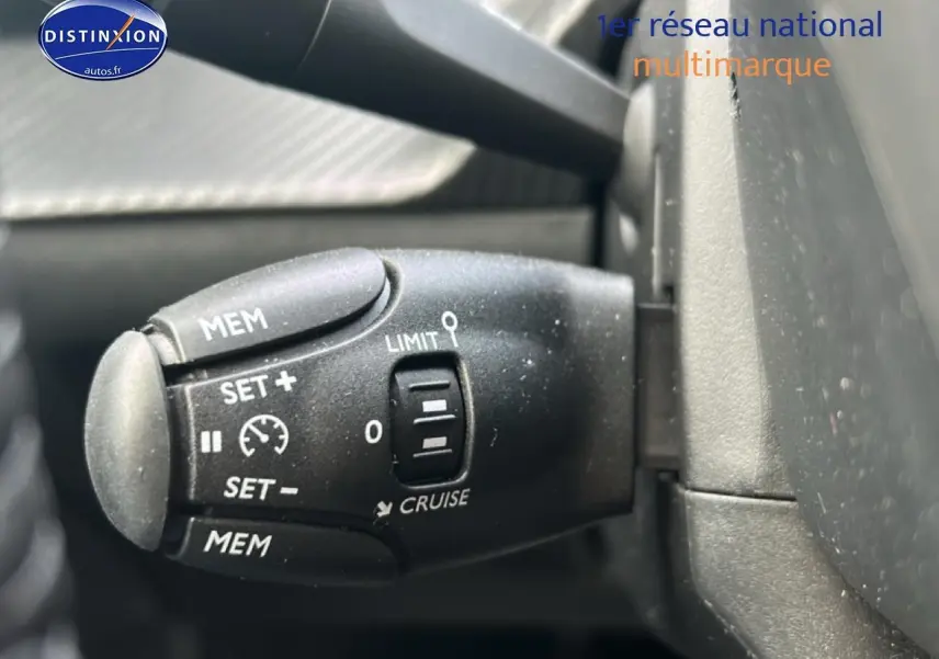 Gros plan sur la commande de régulateur de vitesse noire à gauche du volant dans un Peugeot 208 gris Artense.