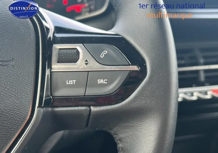 Gros plan sur les commandes au volant gauche en cuir noir de la Peugeot 208 gris artense, avec boutons LIST et SRC visibles.