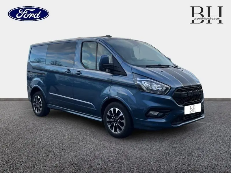 Vue 3/4 avant droit d'un Ford Transit Custom Fourgon bleu azur métallisé avec jantes alu noires et calandre marquée Ford.