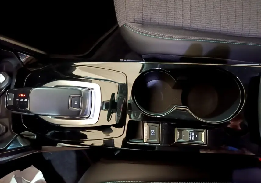 Vue plongeante sur la console centrale noire brillante du Peugeot 2008 orange, avec levier de vitesse automatique et porte-gobelets.