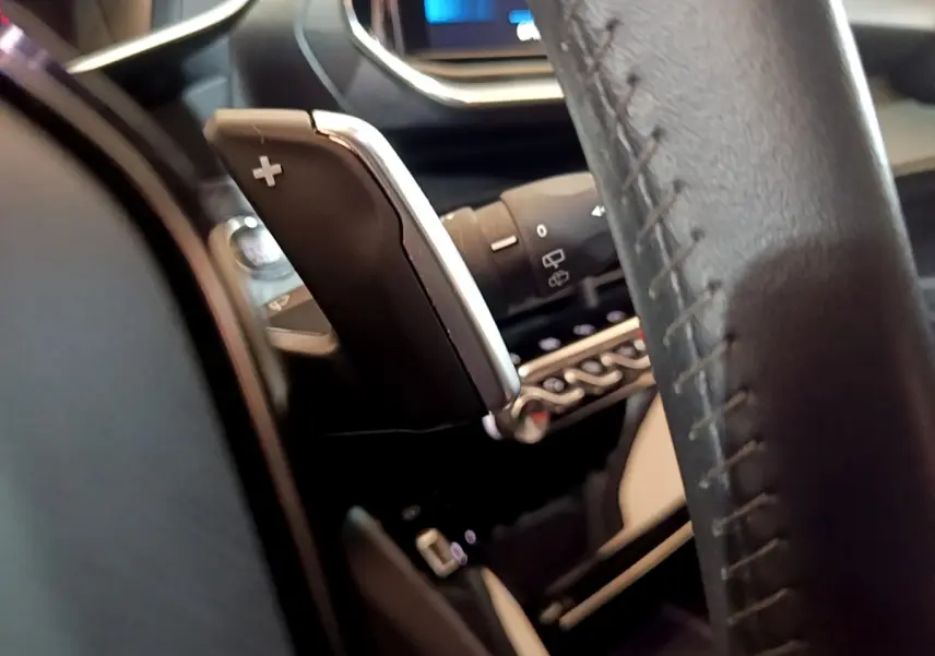 Gros plan sur la palette de changement de vitesse droite en cuir noir, volant et tableau de bord numérique du Peugeot 2008.
