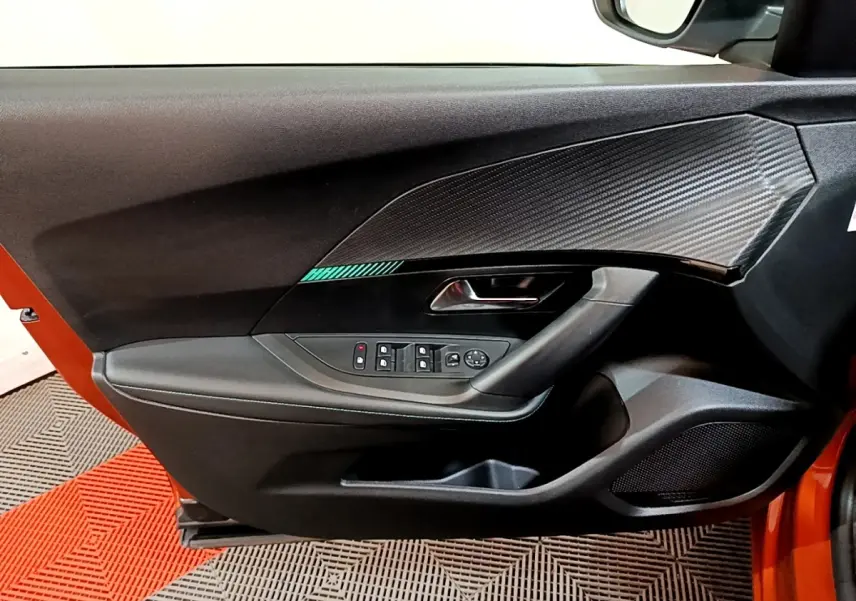 Vue intérieure de la porte avant gauche d'une Peugeot 2008 orange, avec commandes électriques et insert décor carbone.
