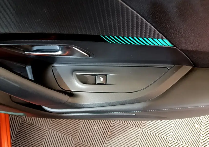 Gros plan sur la portière intérieure côté conducteur d’une Peugeot 2008 orange avec surpiqûres turquoise et bouton de lève-vitre.
