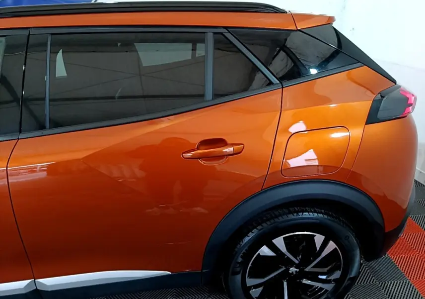 Vue latérale droite sur l’arrière d’un Peugeot 2008 orange métallisé avec jante noire et toit noir contrasté.