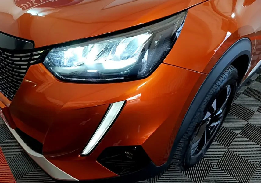 Gros plan sur l'avant droit orange vif du Peugeot 2008 2021, mettant en valeur le phare LED et la calandre noire.