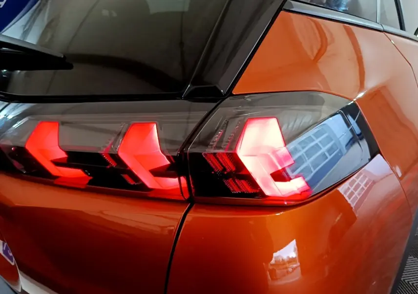 Feu arrière droit allumé d’un Peugeot 2008 orange, vue rapprochée sur la carrosserie et le vitrage noir.