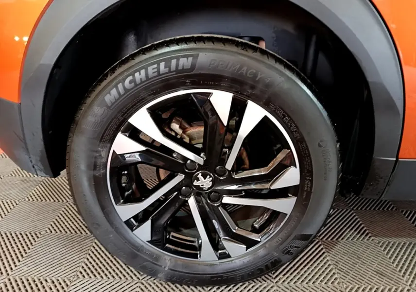 Gros plan sur la roue avant droite d’un Peugeot 2008 orange, jante alliage noire et argent avec pneu Michelin.