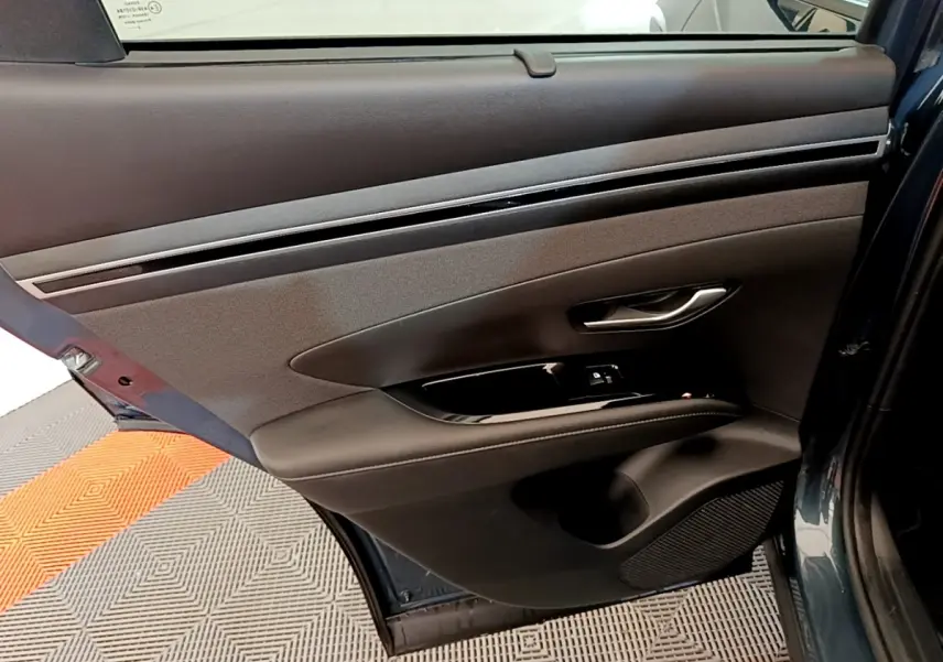 Vue rapprochée de la porte arrière gauche bleu foncé du Hyundai Tucson 2023 avec garniture noire et commande de fenêtre.