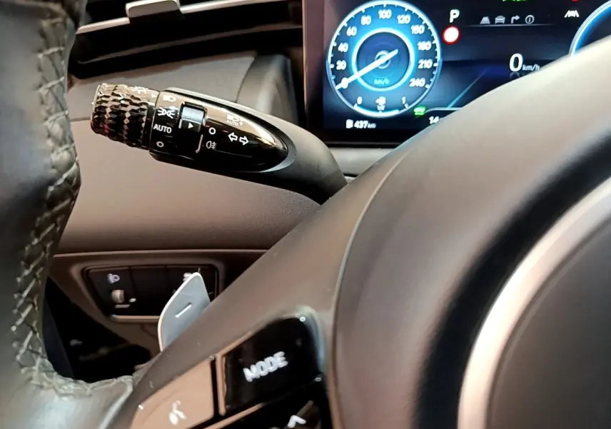 Gros plan sur le volant et la manette de clignotant du Hyundai Tucson bleu, avec tableau de bord numérique allumé en arrière-plan.