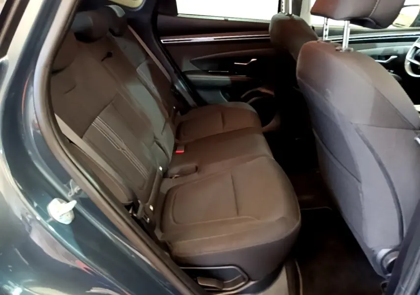 Vue intérieure côté gauche sur les sièges arrière noirs du Hyundai Tucson bleu, avec partie avant et porte ouverte visible.