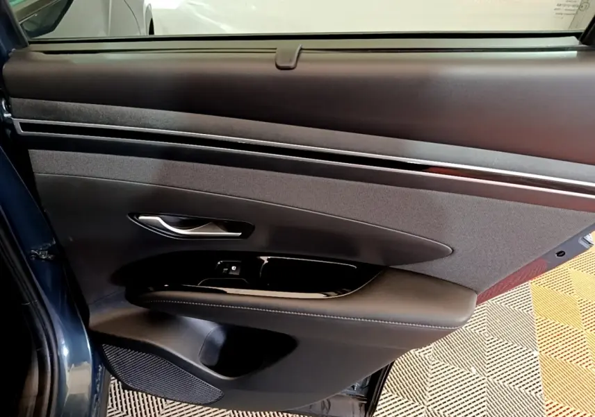 Vue intérieure de la porte arrière gauche bleu foncé du Hyundai Tucson 2023 avec garniture noire et commandes de fenêtre.