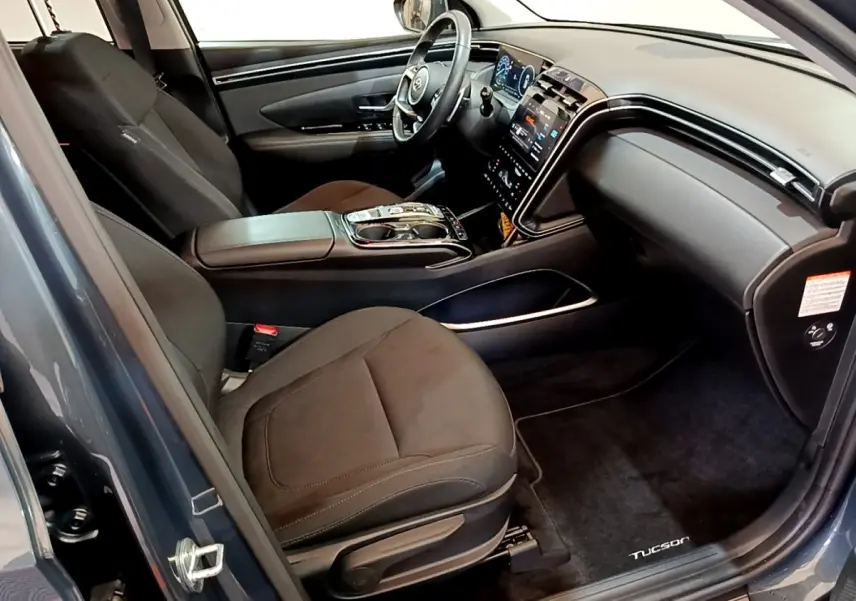 Vue intérieure côté conducteur du Hyundai Tucson bleu 2023, avec tableau de bord digital et console centrale moderne.