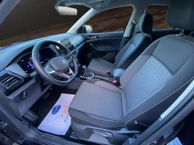 Vue intérieure côté conducteur du Volkswagen T-Cross noir 2025, mettant en valeur le volant multifonctions en cuir et l’écran tactile du tableau de bord.