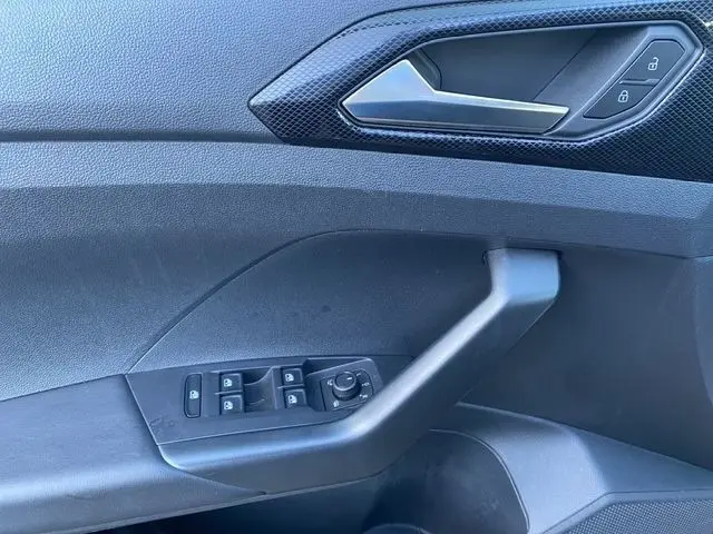 Détail de la porte côté conducteur du Volkswagen T-Cross noir, montrant les commandes des vitres et la poignée intérieure.