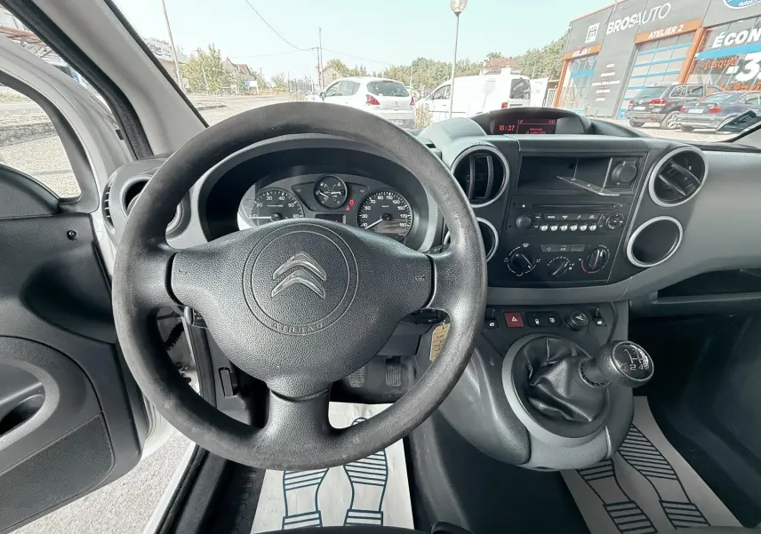 Vue intérieure du tableau de bord et volant noir du Citroën Berlingo blanc, avec levier de vitesses manuel visible.