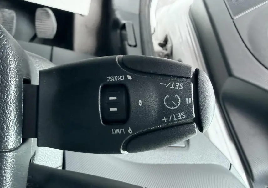 Gros plan sur la commande de régulateur de vitesse noire à gauche du volant dans l’habitacle d’un Citroën Berlingo blanc.