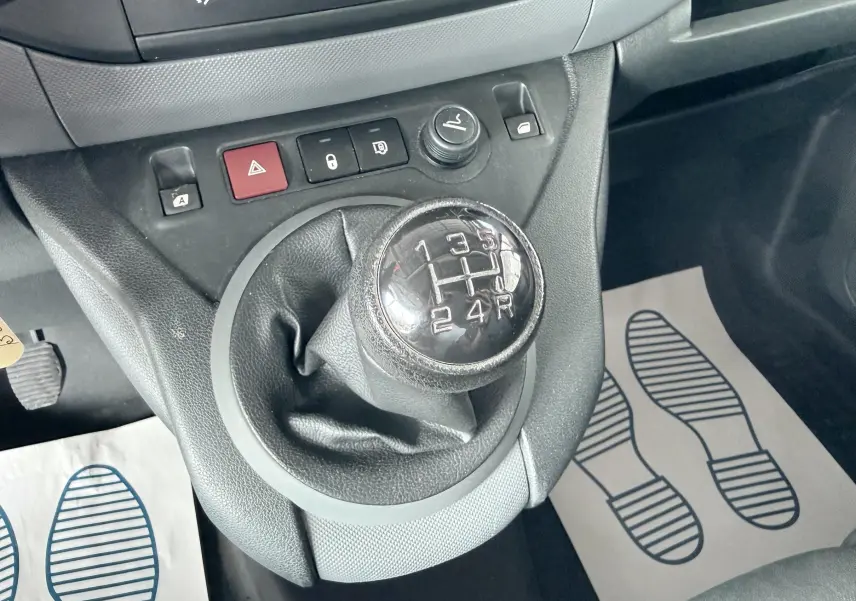 Gros plan sur le levier de vitesses manuel noir du Citroën Berlingo blanc, avec boutons de commande sur la console centrale.