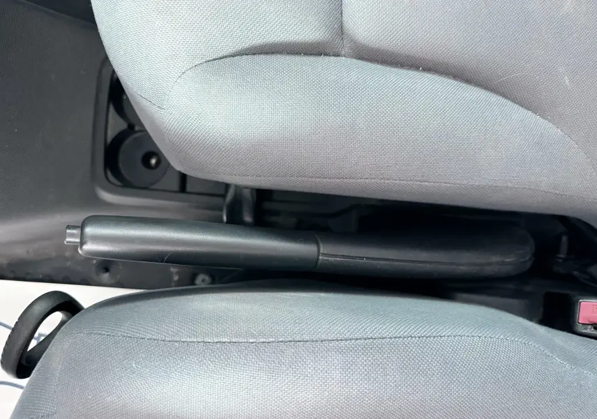 Gros plan sur le frein à main entre les sièges avant en tissu gris du Citroën Berlingo blanc de 2016.