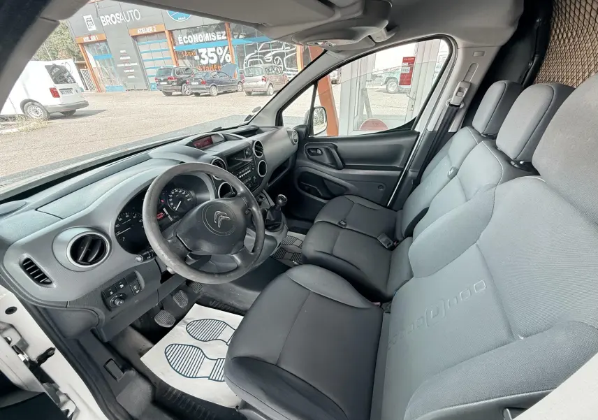 Vue intérieure côté conducteur du Citroën Berlingo blanc, montrant le tableau de bord et les sièges en tissu gris.