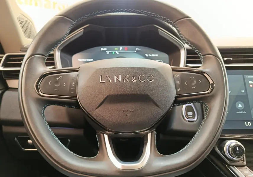 Vue rapprochée du volant noir du Lynk & Co 01 avec commandes tactiles et tableau de bord numérique en arrière-plan.