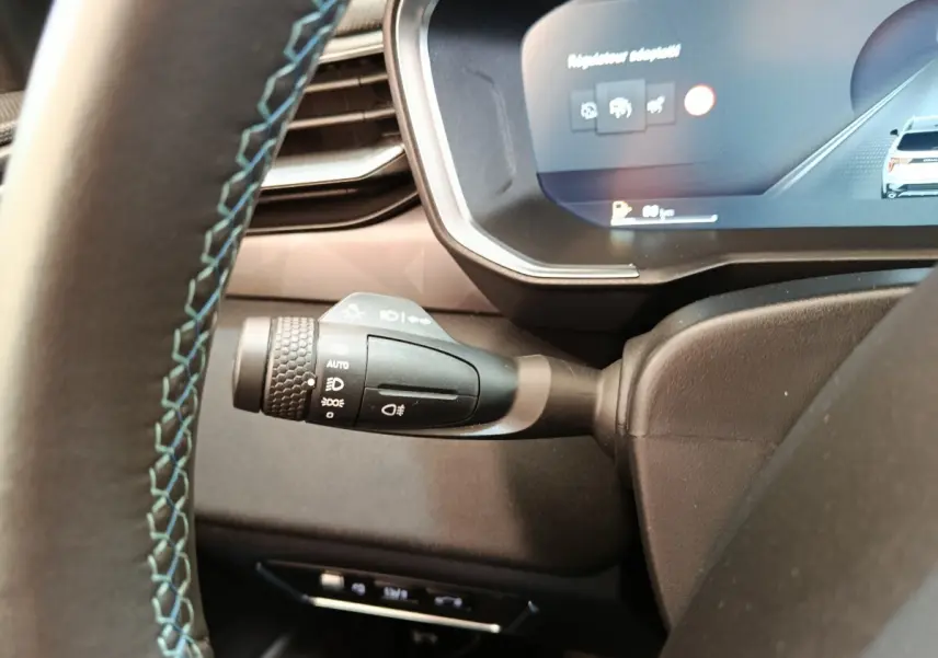 Gros plan sur la commande des phares à gauche du volant cuir noir avec surpiqûres bleues dans le tableau de bord digital du Link & Co 01.