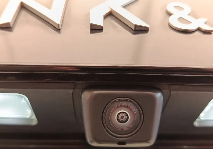 Gros plan sur la caméra de recul intégrée sous le logo LINK & CO, sur un véhicule bleu hybride rechargeable.