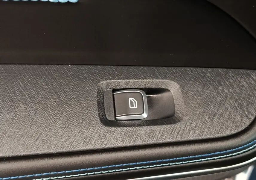 Gros plan sur le bouton de commande de vitre électrique sur la porte intérieure avec surpiqûres bleues du LINK & CO 01 hybride.