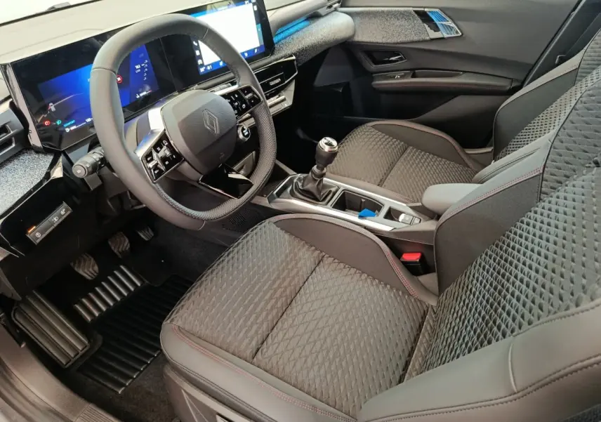 Vue intérieure côté conducteur de la Renault Clio techno TCe 115 essence 2026, avec sièges gris texturés et écran tactile large.