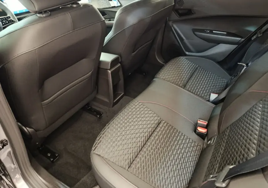 Vue intérieure arrière côté droit de la Renault Clio gris foncé, montrant la banquette avec surpiqûres rouges et l'accoudoir central.