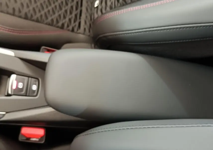 Accoudoir central avant gris foncé avec surpiqûres rouges dans l'habitacle d'une Renault Clio 2026 vue de dessus.