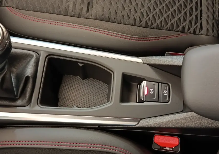 Vue rapprochée de la console centrale de la Renault Clio Techno gris foncé, avec frein à main électrique et surpiqûres rouges.