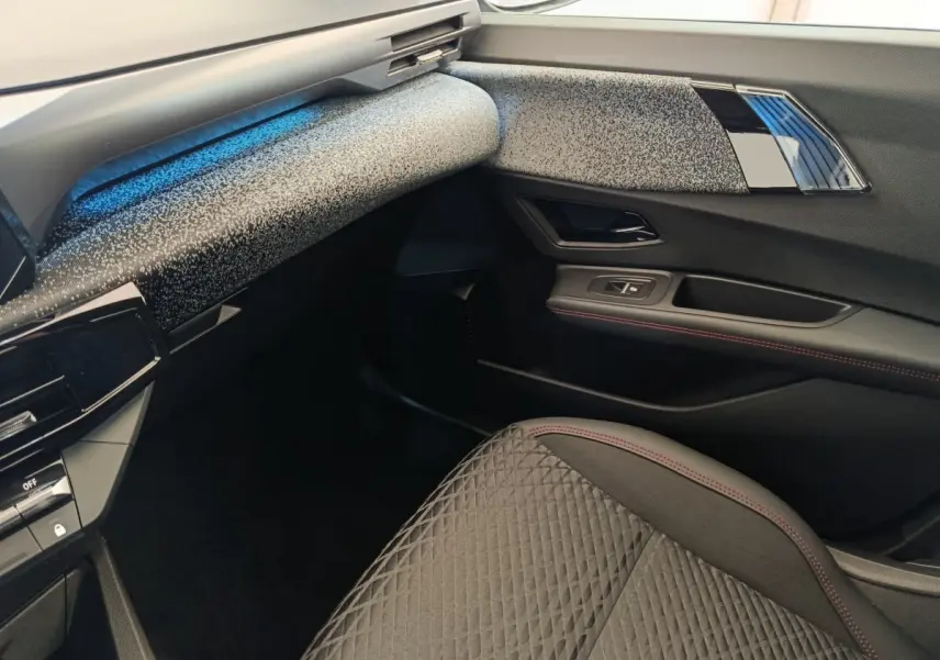 Vue intérieure côté passager avant de la Renault Clio 2026 avec tableau de bord texturé gris et siège tissu noir à surpiqûres rouges.