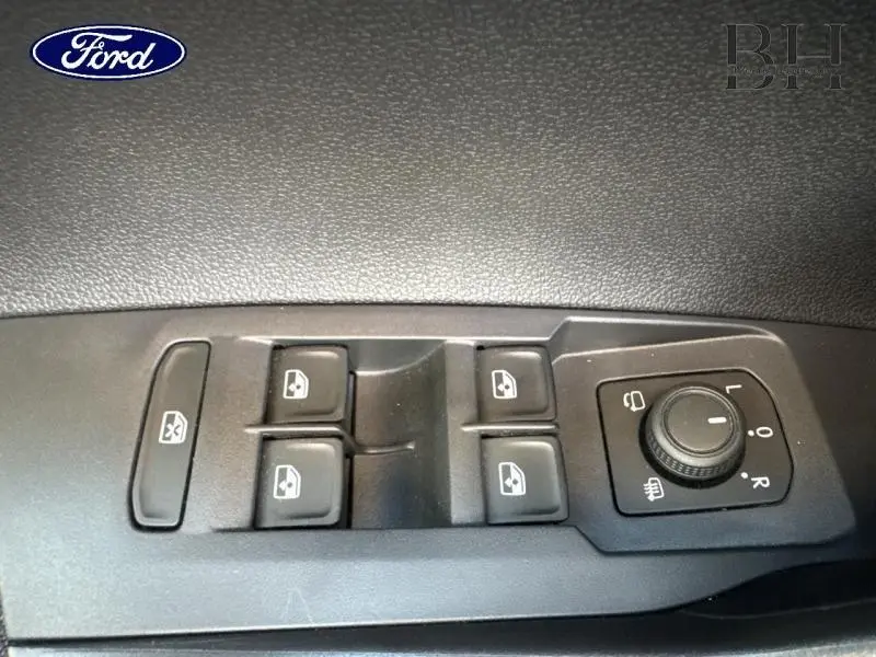 Gros plan sur les commandes de lève-vitres et réglage des rétroviseurs côté conducteur d’un Volkswagen Taigo blanc.