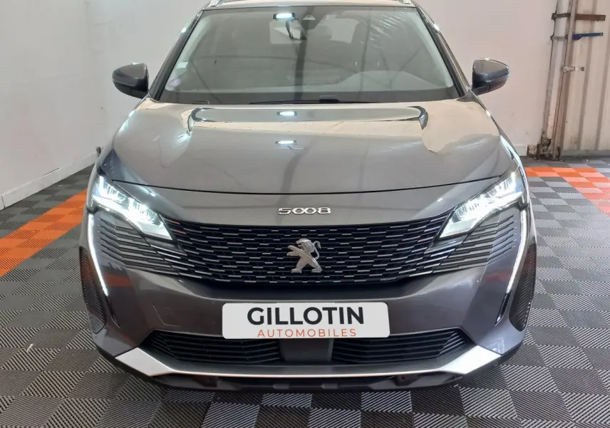 Vue avant d’un Peugeot 5008 gris foncé avec calandre noire et phares LED allumés dans un garage.