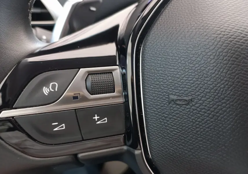 Gros plan sur les commandes vocales et volume du volant cuir noir du Peugeot 5008 gris foncé, version 2021.