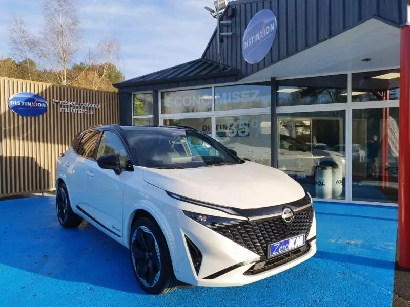 Vue 3/4 avant d'un Nissan Qashqai blanc nacré avec toit noir, stationné devant un showroom Distinxion.