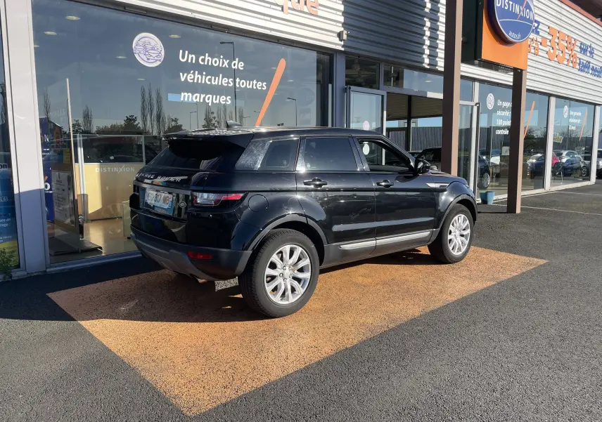 Vue 3/4 arrière droite d'un Range Rover Evoque noir 2016 garé devant une vitrine de concession.