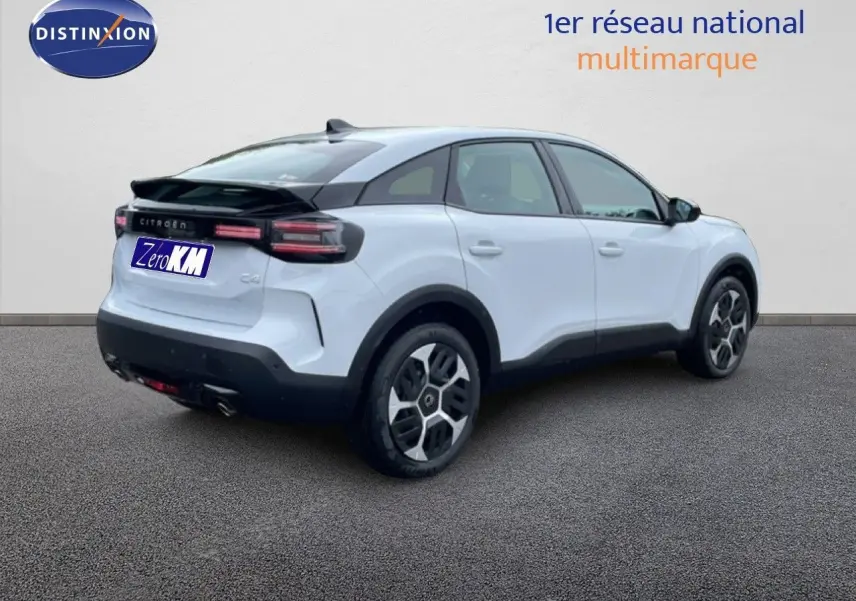 Vue 3/4 arrière droite d'une Citroën C4 blanche métal avec toit noir et jantes distinctives, stationnée sur sol gris.