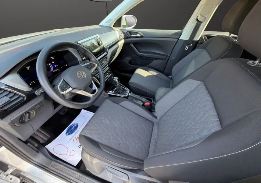 Vue intérieure côté conducteur du Volkswagen T-Cross 2025, montrant le volant cuir, tableau de bord numérique et sièges tissu gris.