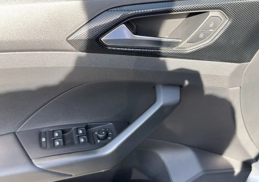 Gros plan sur la porte côté conducteur du Volkswagen T-Cross gris clair, montrant les commandes de vitres et de verrouillage.