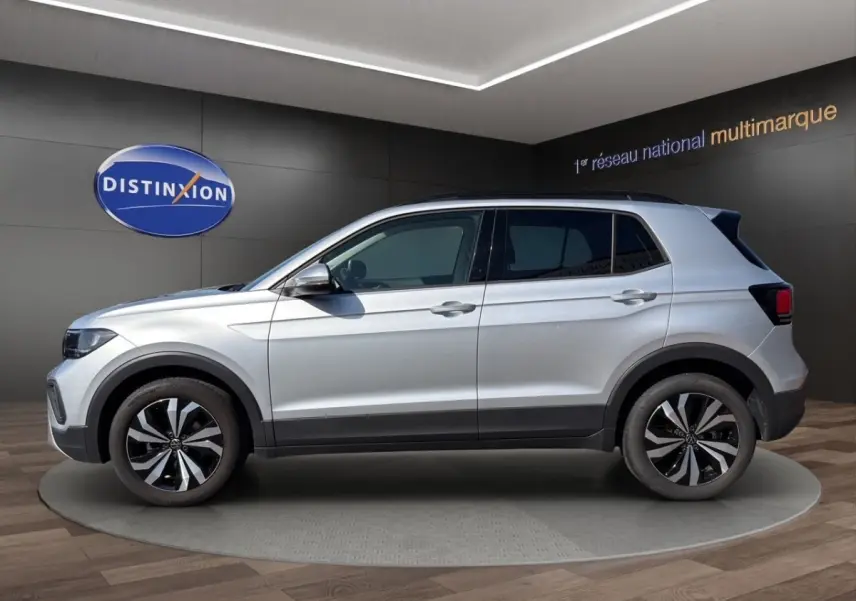 Vue de profil côté gauche d'un Volkswagen T-Cross gris clair avec jantes alliage et barres de toit noires.