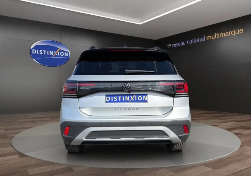 Vue arrière d'un Volkswagen T-Cross gris clair avec feux LED et logo VW visible sur fond showroom.