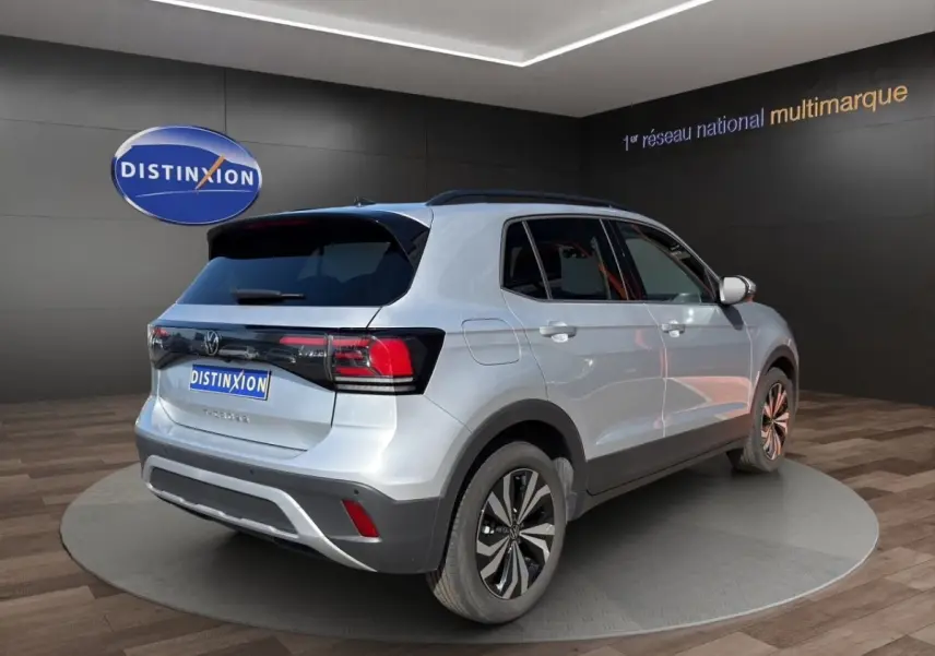 Vue 3/4 arrière droite du Volkswagen T-Cross gris clair 2025 avec jantes alliage et toit noir en showroom.