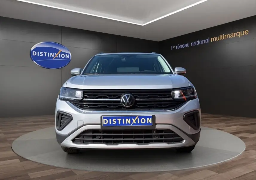 Vue de face du Volkswagen T-Cross gris clair 2025 avec calandre noire et logo VW centré, en showroom.