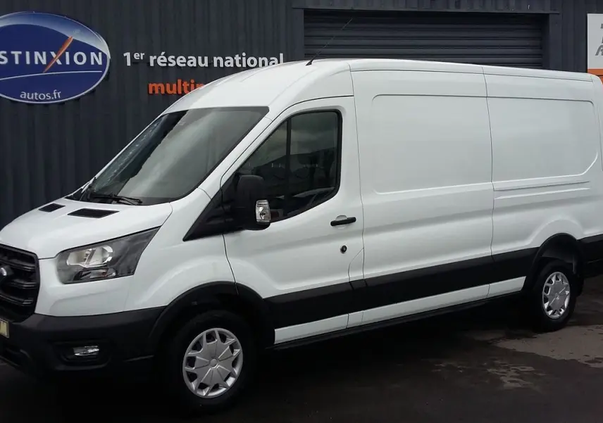 Fourgon Ford Transit blanc glacier vu de profil côté gauche, avec pare-chocs et bas de caisse noirs sur sol humide.