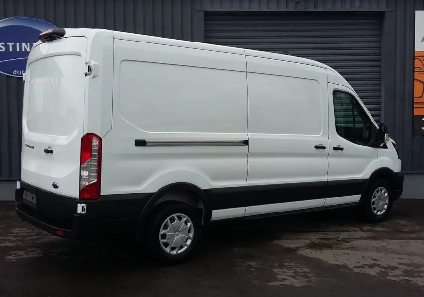 Fourgon Ford Transit blanc glacier vu en 3/4 arrière côté gauche, avec protections noires et jantes acier.