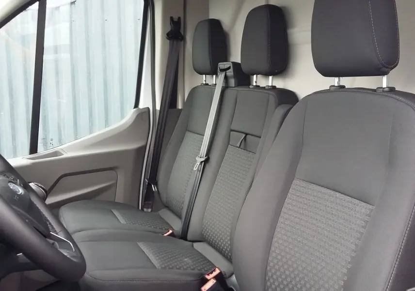 Vue intérieure côté conducteur du Ford Transit Fourgon blanc glacier 2022, sièges tissu gris avec appuie-têtes et ceintures visibles.