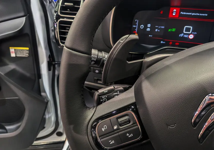 Vue rapprochée du volant noir du Citroën C5 Aircross hybride 2025 avec porte avant gauche ouverte et tableau de bord numérique.
