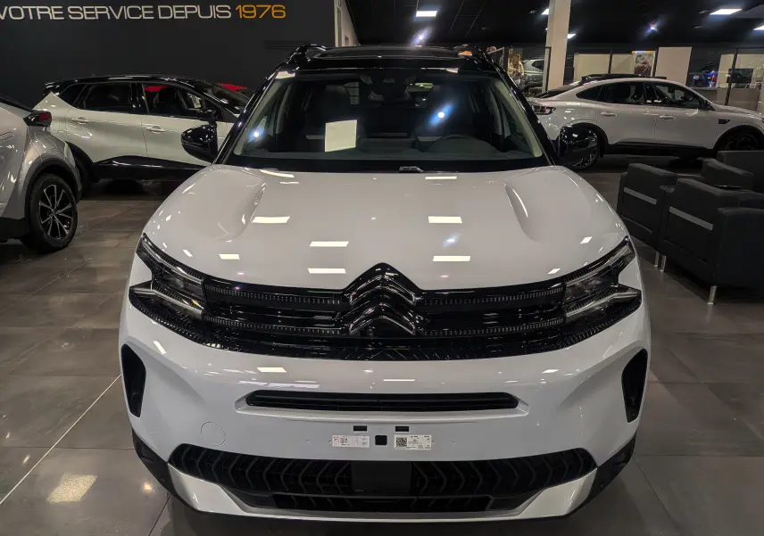 Vue de face du Citroën C5 Aircross hybride blanc Okénite avec toit noir brillant dans un showroom moderne.