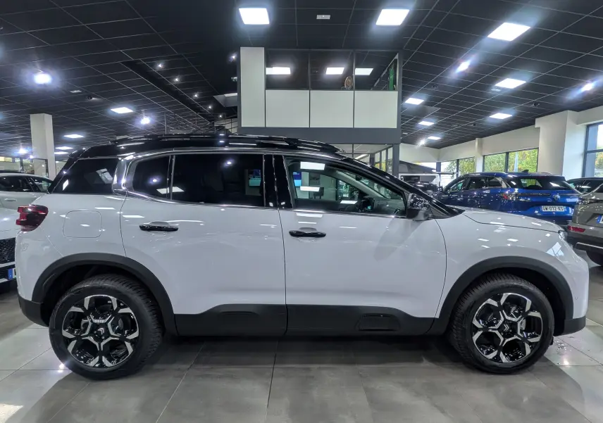 Profil latéral droit d'un Citroën C5 Aircross hybride blanc Okénite avec toit noir dans un showroom lumineux.